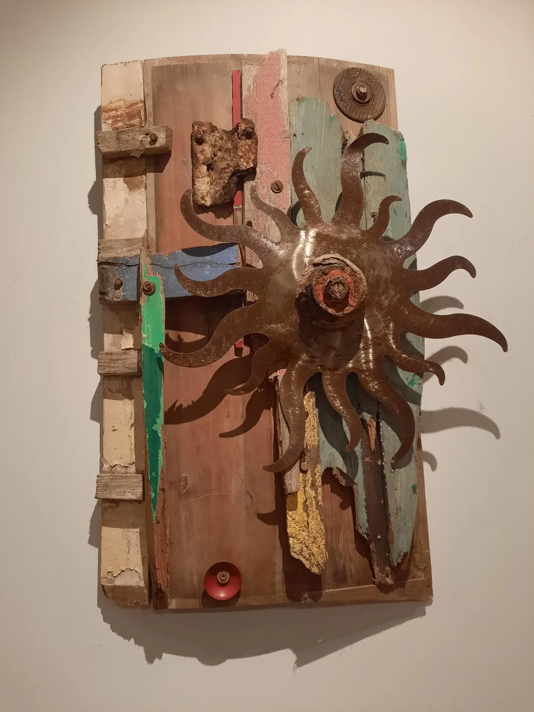 Wall piece of weathered wooden boards, painted strips and metal fittings around a rusted metal sun